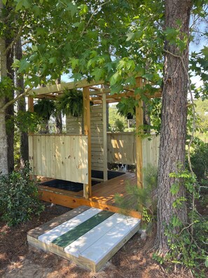 A wooden deck with a pergola structure, surrounded by trees and greenery.