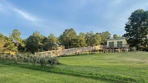 A grassy field with a wooden deck and a building in the background. - Air conditioned Glamping Tent overlooking a beautiful orchard (Merritt)