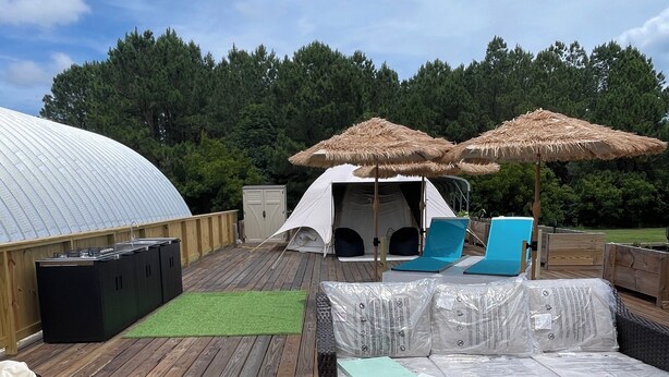 A covered outdoor area with a wooden deck, a tent, two lounge chairs, and a colorful striped rug. - Air conditioned Glamping Tent overlooking a beautiful orchard (Merritt)