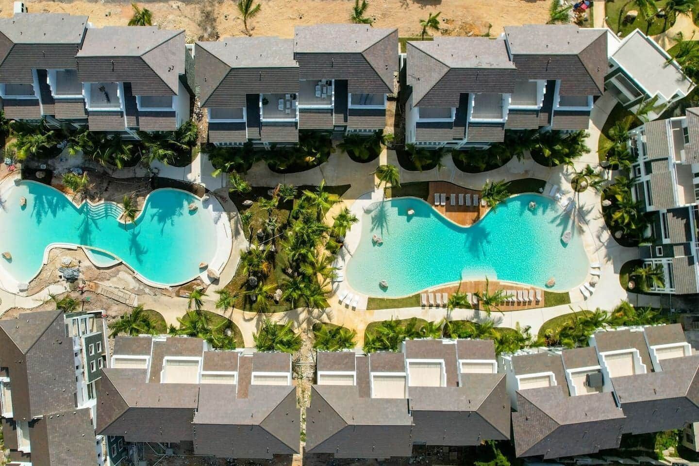 A resort with multiple buildings, two swimming pools, and a sandy beach.