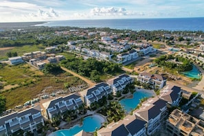 Eine Luftaufnahme eines Küstenresorts mit mehreren Gebäuden, einem Schwimmbecken und Blick aufs Meer.