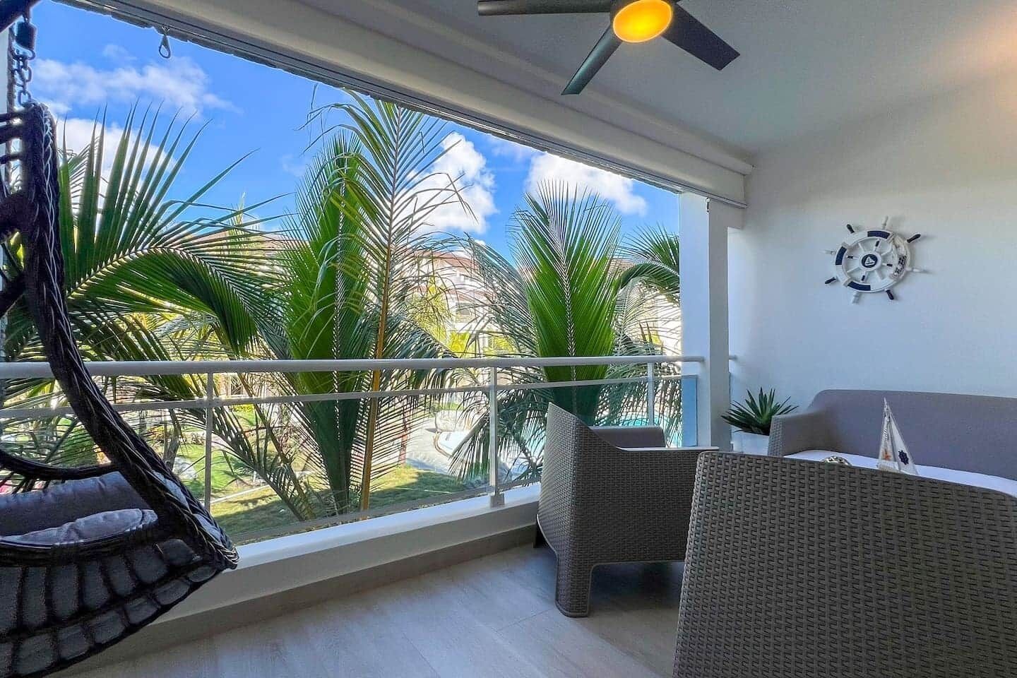 Een balkon met uitzicht op palmbomen, een plafondventilator en rieten meubilair.