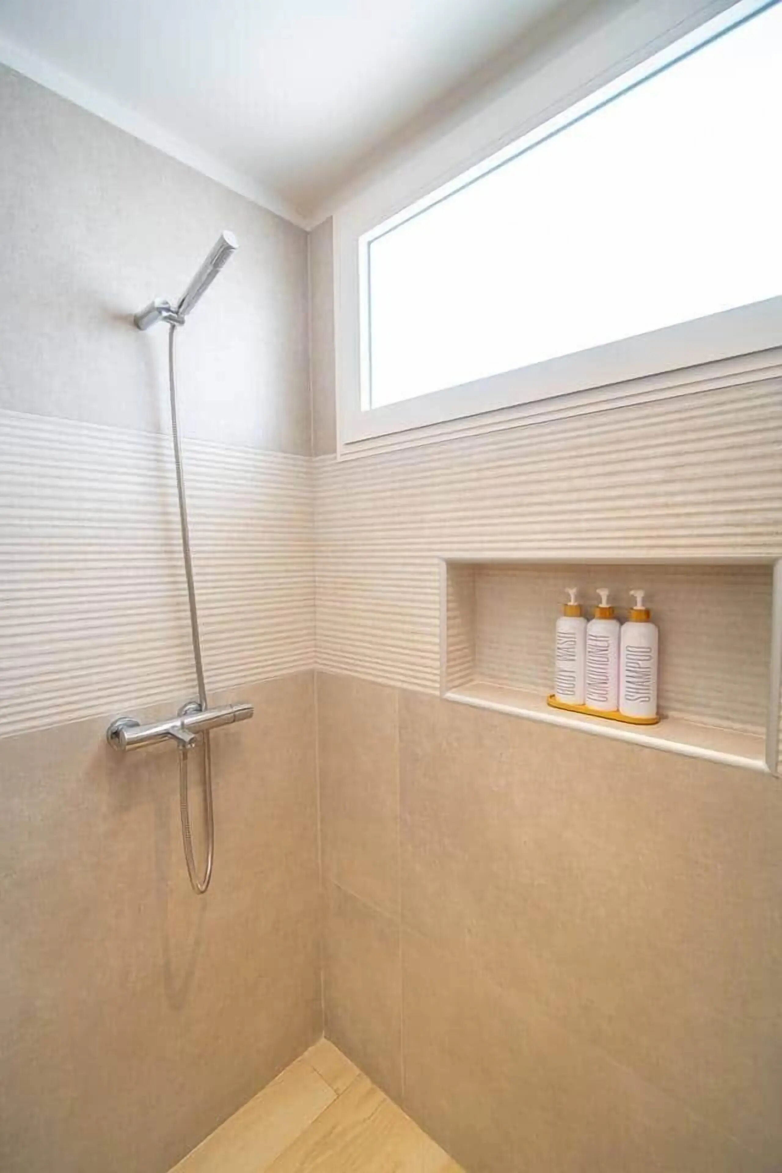 A shower with a handheld showerhead, a wall-mounted faucet, and a shelf with toiletries.
