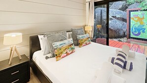 Een hotelkamer met een bed, kussens, een nachtkastje, een lamp en uitzicht op rotsen en groen.