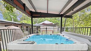 Een jacuzzi met een metalen reling, omringd door een overdekt terras met uitzicht op een huis op de achtergrond.