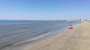 A beach with clear water, a sandy shore, and buildings in the distance. - 2 rooms sea view Boucanet parking beaches 200m away (LE GRAU DU ROI)