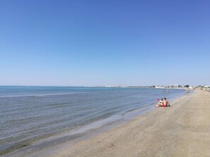 A beach with clear water, a sandy shore, and buildings in the distance. - 2 rooms sea view Boucanet parking beaches 200m away (LE GRAU DU ROI)
