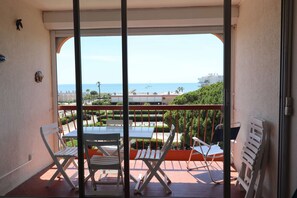 Ein Balkon mit Tisch und Stühlen, Blick auf das Meer und ein Gebäude im Hintergrund.