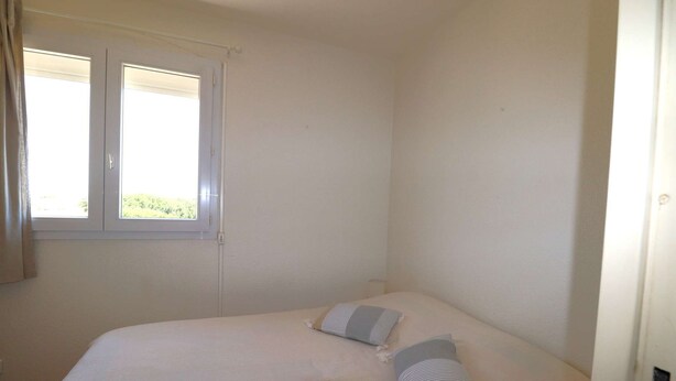 A bedroom with a bed, two pillows, a window, and a door. - 2 rooms sea view Boucanet parking beaches 200m away (LE GRAU DU ROI)