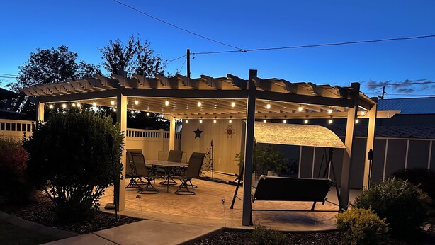 A covered patio area with a table and chairs, string lights, and a pergola. - The Gathering Place - Large home, 6 bedrooms, 11 beds, beautiful fenced backyard (Vernal)