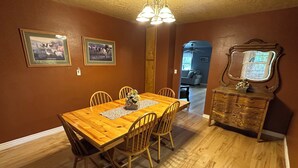 A dining room with a wooden table, chairs, a floral centerpiece, and a mirror on a dresser. - The Gathering Place - Large home, 6 bedrooms, 11 beds, beautiful fenced backyard (Vernal)