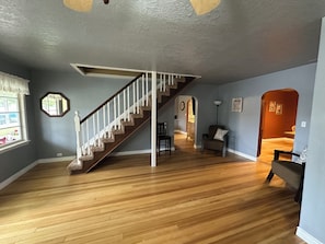 Una habitación amplia con una escalera de madera, un ventanal con vistas y una zona de estar acogedora.