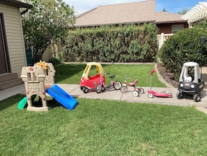 A residential driveway with a children's play area including a slide and various toys. - The Gathering Place - Large home, 6 bedrooms, 11 beds, beautiful fenced backyard (Vernal)