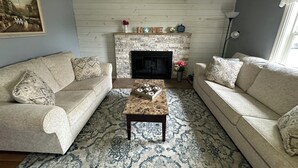 A living room with two sofas, a coffee table, a fireplace, and a painting on the wall. - The Gathering Place - Large home, 6 bedrooms, 11 beds, beautiful fenced backyard (Vernal)