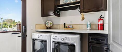 A laundry area with two front-loading washers, a shelf with a starfish decoration, a fire extinguisher, and a view of the outside.
