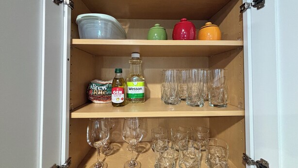 Un armario de cocina con estantes que contienen utensilios, botellas y vasos.