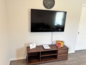 Un televisor de pantalla plana montado en la pared, un mueble de madera debajo y una puerta a la derecha.