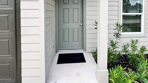 Una casa residencial con puerta gris, buzón y un pequeño jardín con plantas verdes.