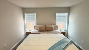 Un dormitorio con cama, dos mesitas de noche con lámparas y una ventana con persianas.