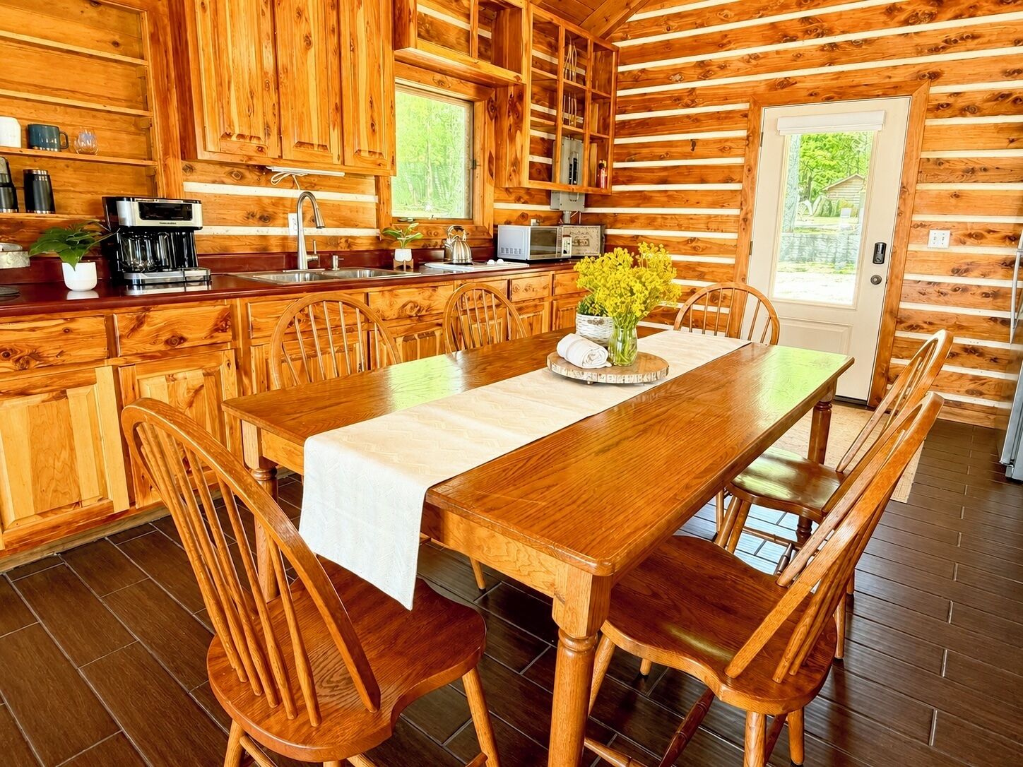 L’intérieur d’un chalet en bois comprend une table à manger, des chaises, un coin cuisine équipé d’appareils électroménagers et une fenêtre.