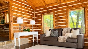 A log cabin interior with a sofa, table, and windows. - One Bedroom Cabin with Panoramic View at Paul's Point (Altamont)