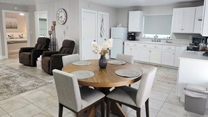 A modern living room with a dining table, two sofas, and a kitchen area with white cabinets and appliances.