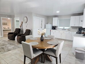 Una sala moderna con una mesa de comedor, dos sofás y una zona de cocina con armarios y electrodomésticos blancos.