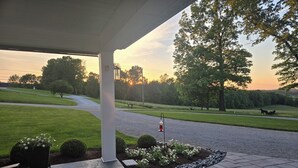 A covered patio with a view of a road and trees.