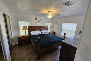 Une chambre à coucher avec un lit en bois, deux tables de chevet, un ventilateur de plafond et des appliques murales.