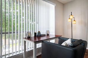 A room with a view through large windows, a table with decorative items, a sofa, and a floor lamp.