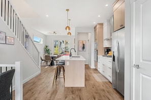 A modern kitchen with a central island, stainless steel appliances, and a staircase with black railings. - Sunlit Slate, 3BR+Bonus+XBOX+BBQ with Modern Design + Private Deck (Calgary)