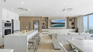 Uma cozinha moderna com uma ilha central, banquetas de bar e uma área de jantar com uma grande janela com vista para uma paisagem deslumbrante.