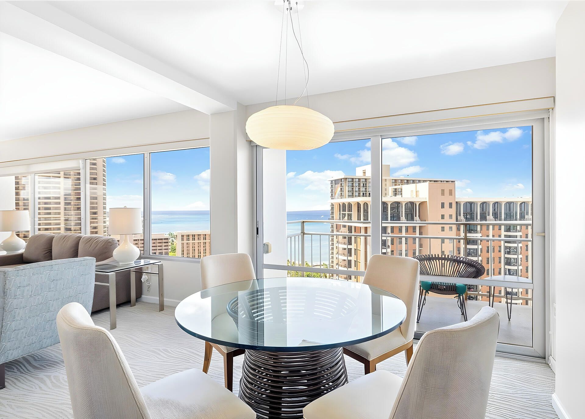 Sala de estar moderna com mesa de vidro, assentos confortáveis e vista para o horizonte urbano através de grandes janelas.