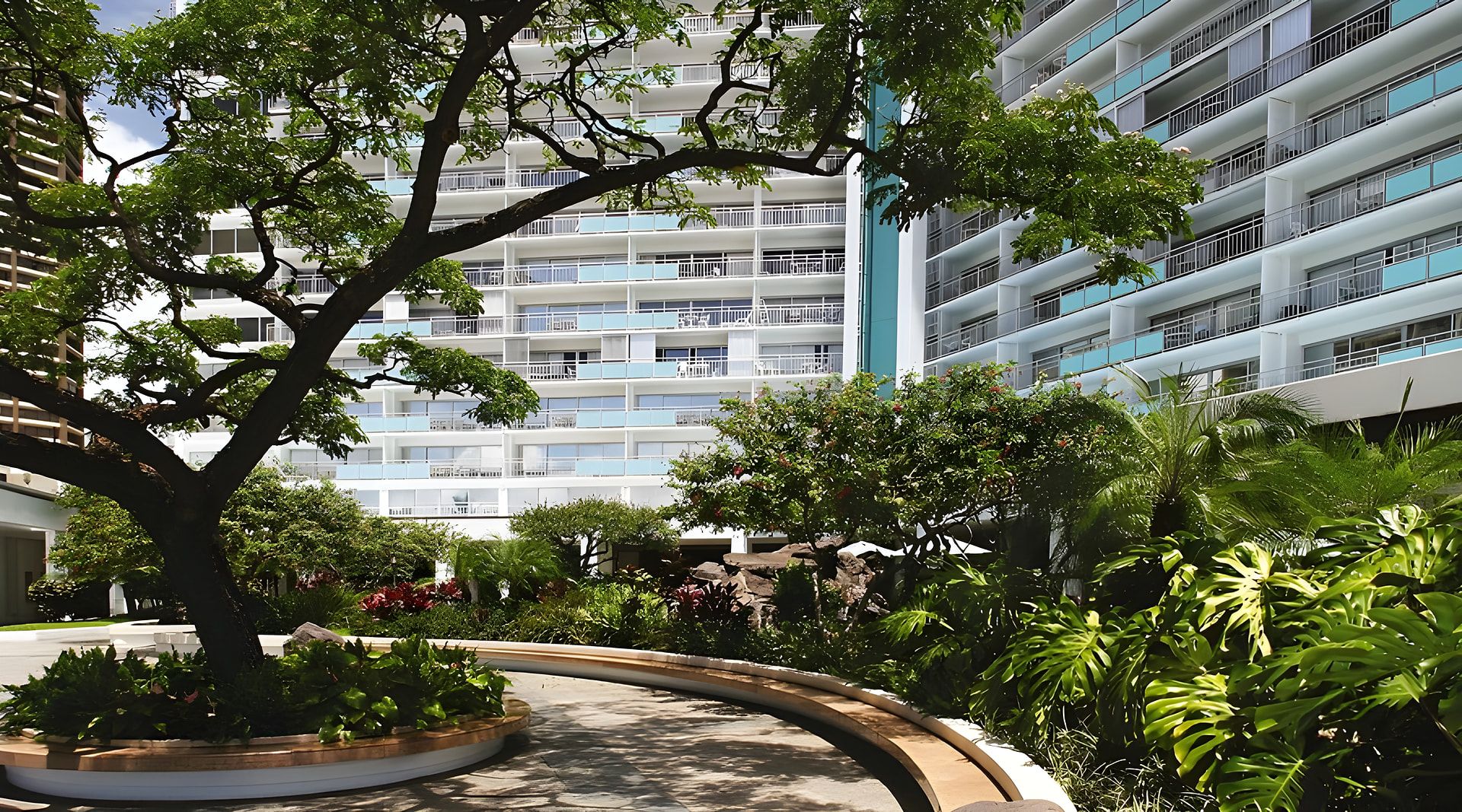 Un edificio moderno con varios balcones y un patio ajardinado con árboles y plantas.