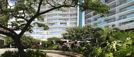 Un edificio moderno con varios balcones y un patio ajardinado con árboles y plantas.