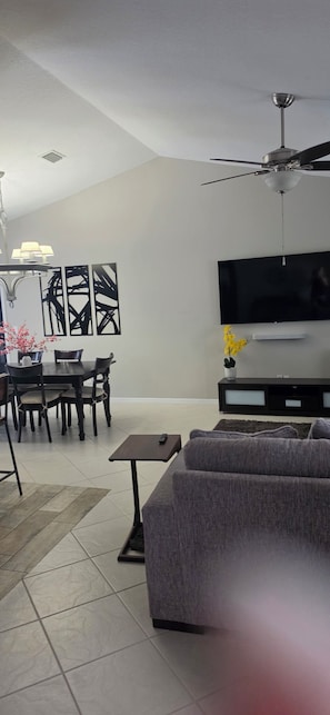 Ein modernes Wohnzimmer mit Flachbildfernseher, Deckenventilator, Essbereich mit Tisch und Stühlen sowie einer Couch.