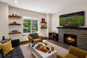 A living room with a fireplace, a television displaying a football game, and a snack table. - Downtown McCall Retreat | Walk Everywhere (McCall)