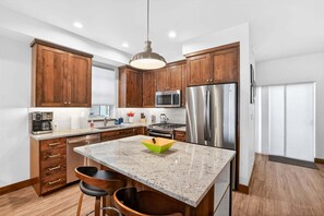 A modern kitchen with wooden cabinets, stainless steel appliances, a granite countertop, and a pendant light. - Downtown McCall Retreat | Walk Everywhere (McCall)