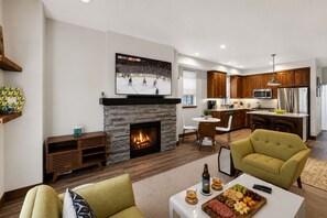 A living room with a fireplace, a television, and a dining area with a kitchen in the background. - Downtown McCall Retreat | Walk Everywhere (McCall)