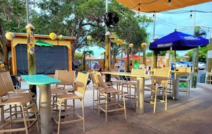 Espace extérieur aménagé avec des chaises et des tables en osier, un espace couvert orné d’une enseigne Bud Light et un espace clos agrémenté de diverses décorations.
