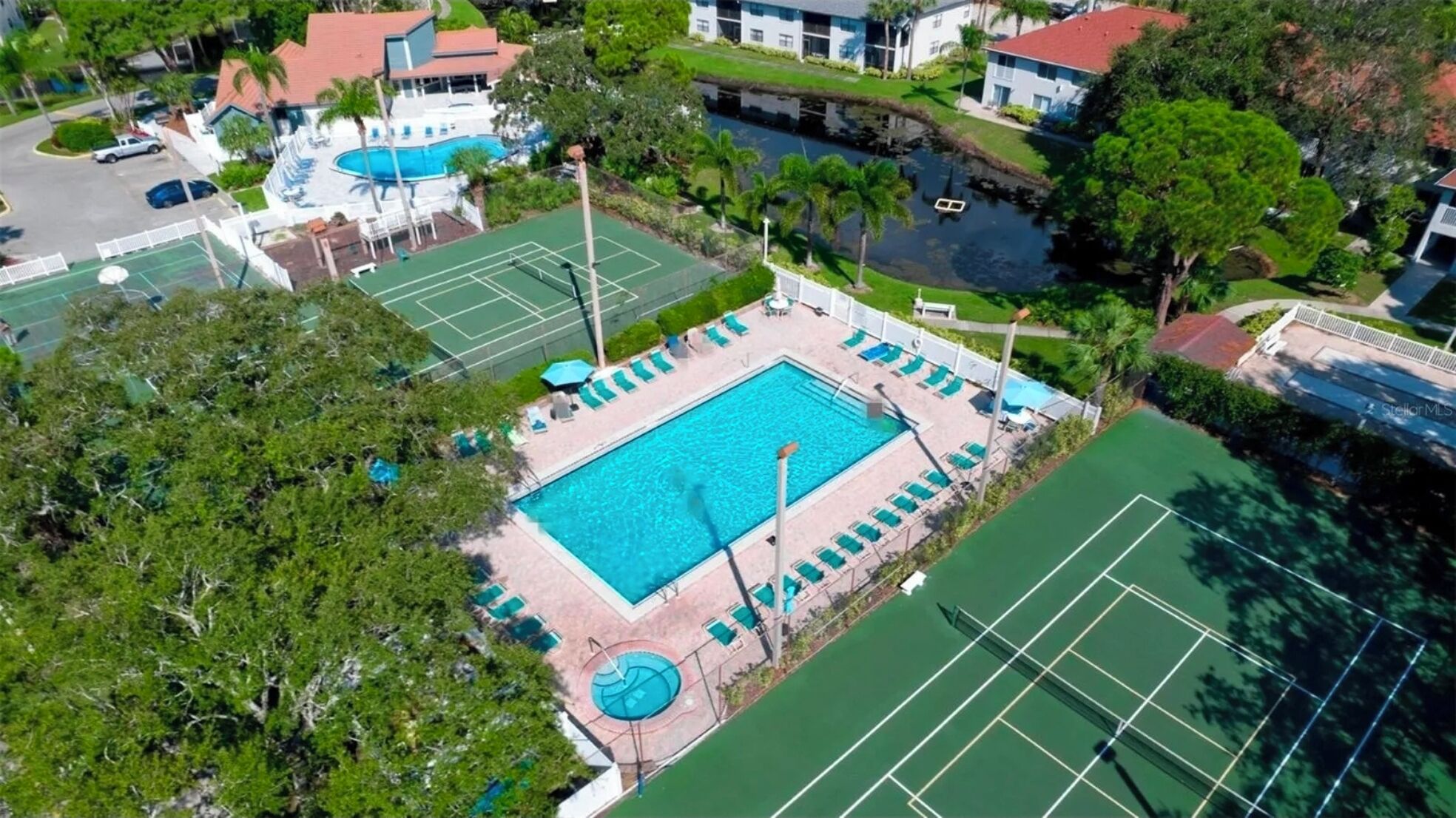 An aerial view of a property with a swimming pool, tennis courts, and a small boat on a waterway.