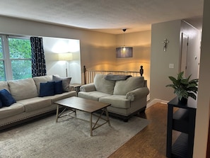 A living room with a sofa, armchair, coffee table, and a potted plant.