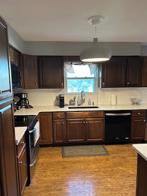 A kitchen with wooden cabinets, a window, a sink, a stove, and a dishwasher.