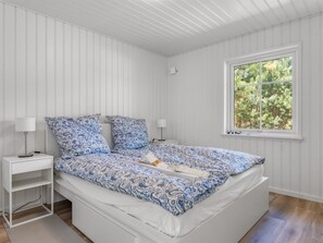 Un dormitorio con una cama, dos mesitas de noche, un ventanal y vistas a árboles.
