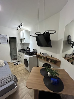 Ein kompakter Wohnraum mit Küchenzeile, einem Bett, einer Essecke und einem Wand-Fernseher.