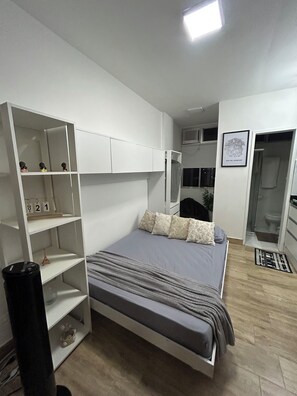 Ein Schlafzimmer mit einem Bett, einem weißen Kleiderschrank, einer kleinen Mülltonne und einer Duschkabine.