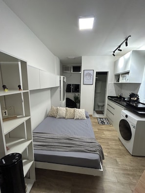 Ein kleines Schlafzimmer mit Bett, Waschmaschine und einer Küchenzeile.