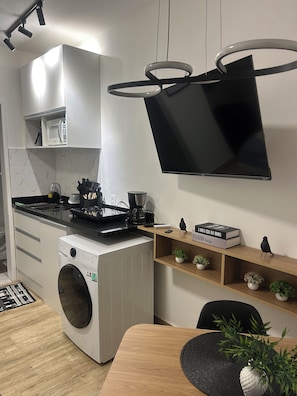 Eine moderne Küche mit Waschmaschine, Mikrowelle, Kaffeemaschine und einem an der Wand befestigten Flachbildfernseher.