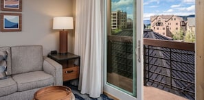 Habitación de hotel con sofá, lámpara, ventana con cortinas y vistas a edificios.