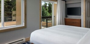 Un dormitorio con una cama grande, un televisor en la pared y un balcón con barandilla.